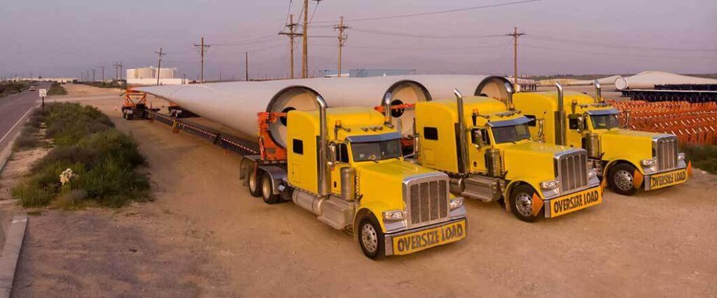 Three yellow semis performing out of gauge cargo shipping