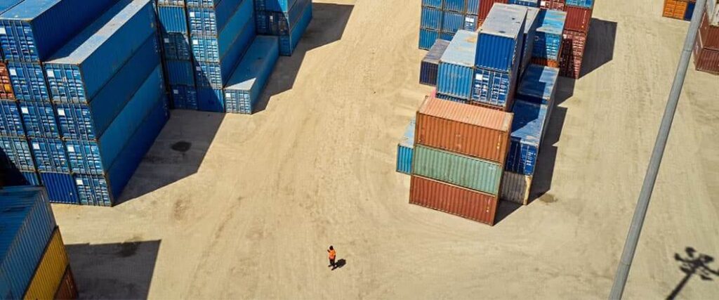 A port worker standing near some cargo containers while considering the benefits of FCL shipping